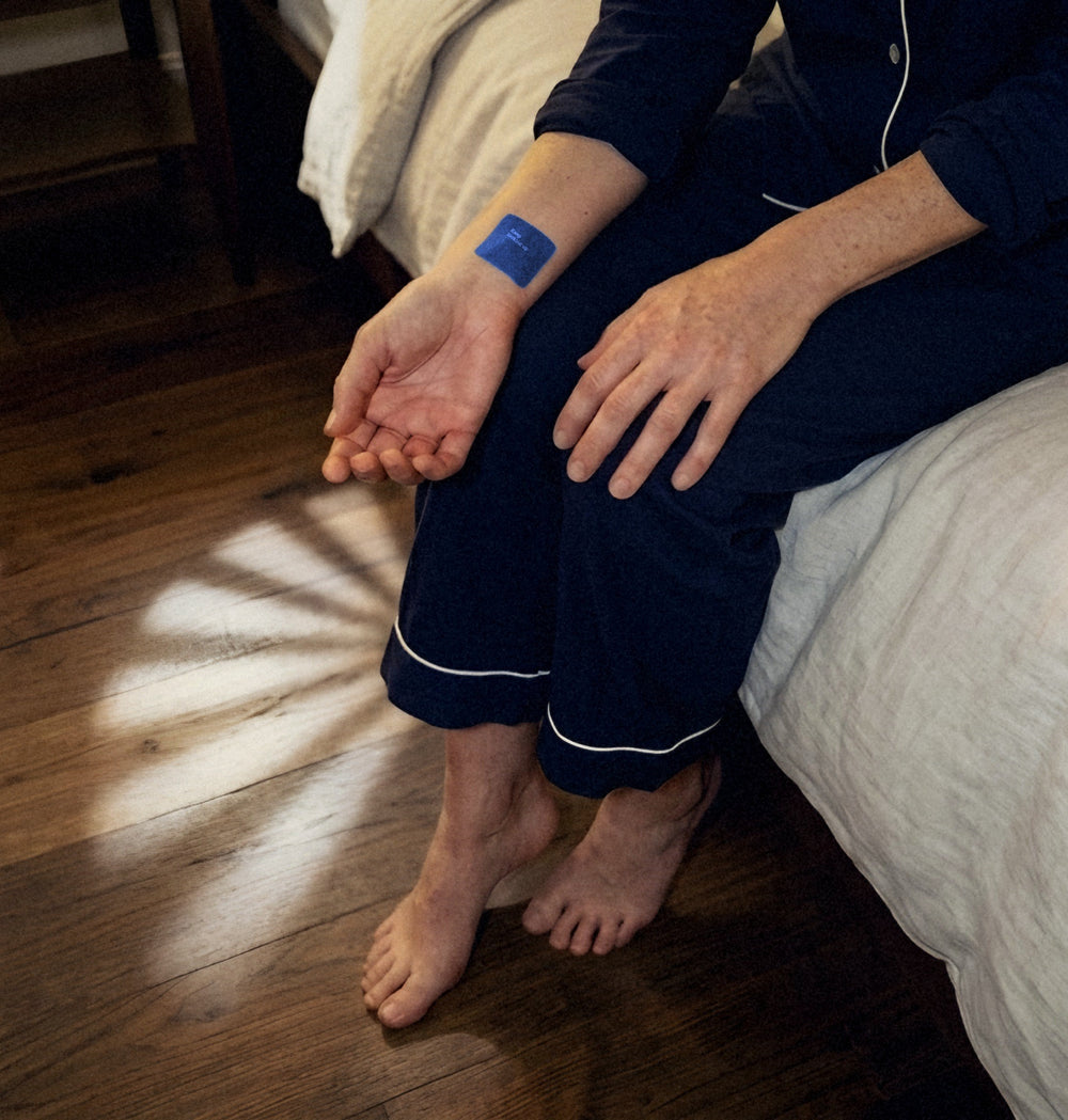 Sitting on the edge of the bed in navy pyjamas, a small blue patch on the inside of the wrist, moonlight across the floorboards.
